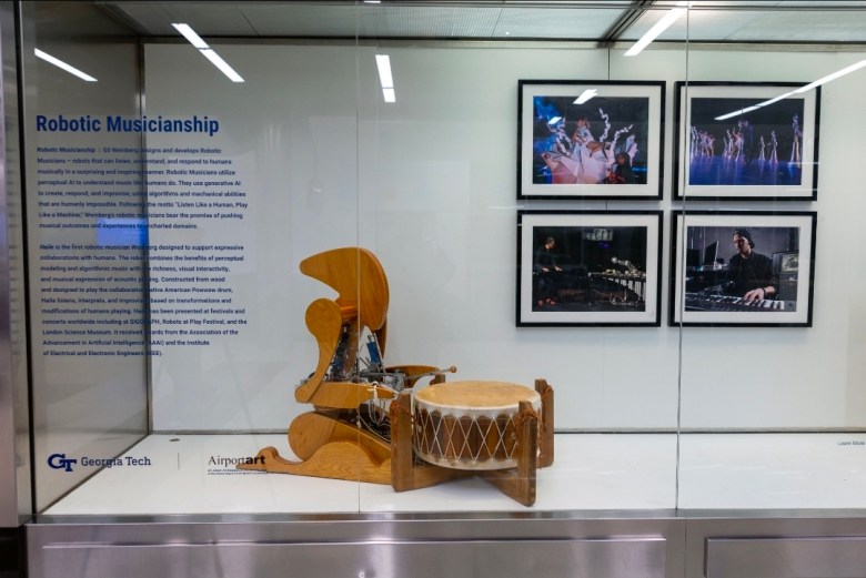 Haile robotic drummer displayed in a glass case with explanatory text and performance photos as part of Georgia Techโs airport exhibition.