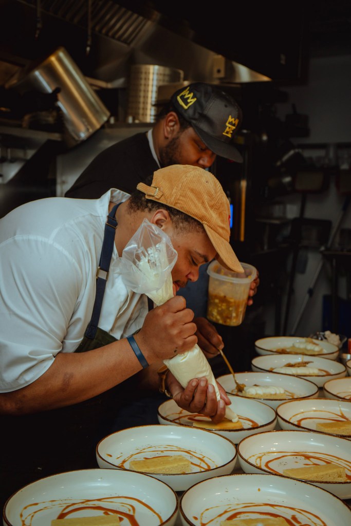 Chefs Robert Butts (front) and Gary Caldwell (back) plating dishes for a New South dinner. (Courtesy of Laureen Lynn and Aaila Avani)