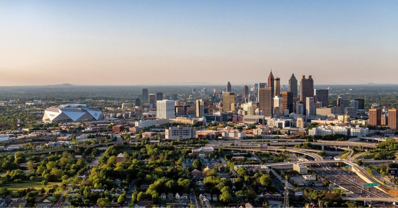 Distance shot of downtown Atlanta, including skyscrapers, Interstate 75, and the Mercedes-Benz stadium. 