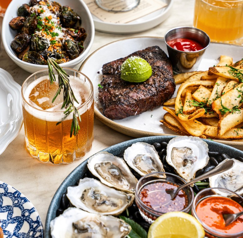 A table spread at Luella in Atlanta with oysters, steak, brussels sprouts, fries, and cocktails. 