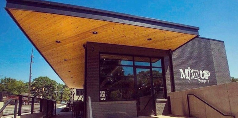 The black brick exterior with triangular roof jutting out of Mix'd Up Burgers in East Lake on a sunny blue sky day.