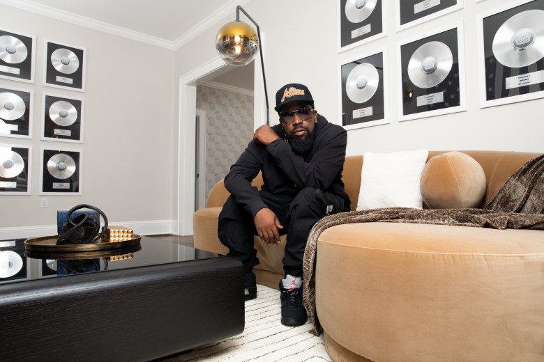 OutKast member Big Boi sits facing the camera, surrounded by platinum records mounted on the walls.
