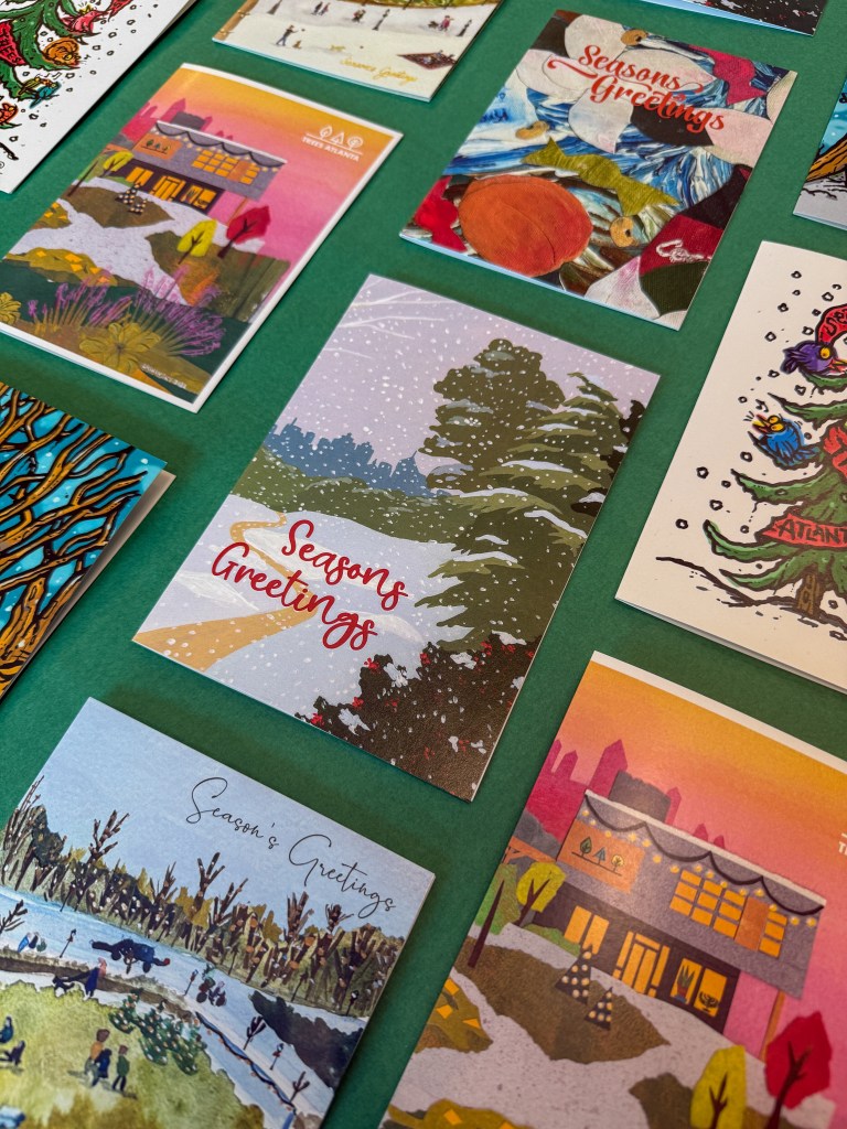 Flat lay of assorted Trees Atlanta holiday cards, including Elizabeth Lang’s snowy evergreen landscape titled Evergreen.