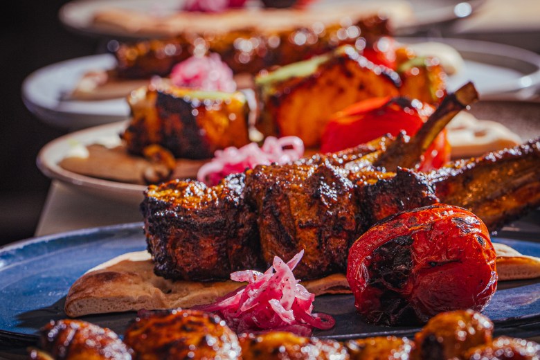Shot of lamb chops, grilled tomato, and Persian flat bread on a blue ceramic plate. 